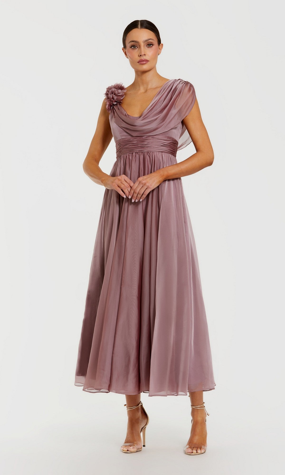 A woman stands against a plain white background wearing the Mac Duggal 68967 Tea-Length Party Dress in Antique Rose, featuring a sleeveless fit-and-flare silhouette with a floral accent on one shoulder, paired with strappy nude heels.